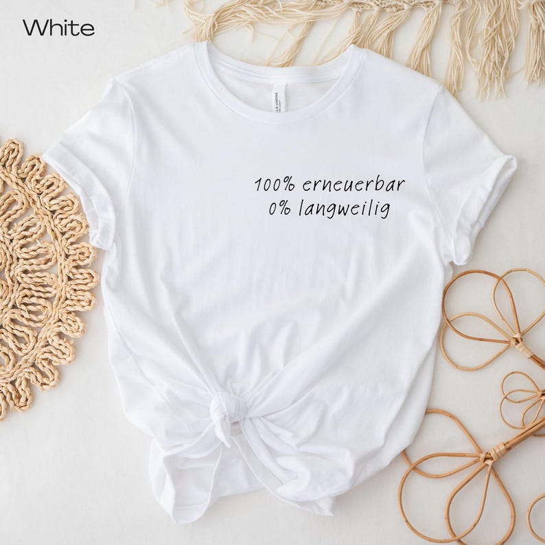 Puede incluir: Camiseta blanca con el texto "100% erneuerbar 0% langweilig" en escritura negra. La camiseta est&aacute; anudada a la cintura. La camiseta est&aacute; sobre una superficie blanca con elementos decorativos.
