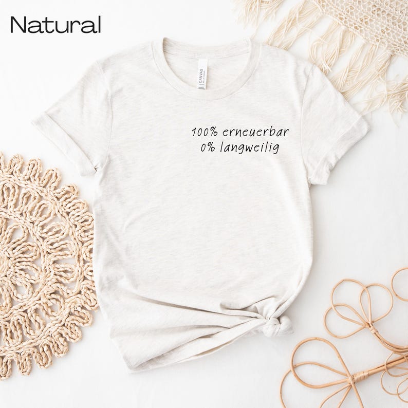 Puede incluir: Una camiseta de color claro con el texto "100% erneuerbar 0% langweilig" en escritura negra. La camiseta est&aacute; anudada en la parte inferior y tiene mangas cortas. La palabra "Natural" est&aacute; impresa en la parte superior izquierda.