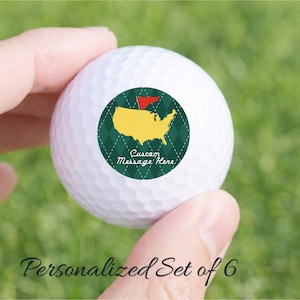 Puede incluir: Pelota de golf blanca con un diseño verde y amarillo que presenta un mapa de los Estados Unidos y una bandera roja. La pelota tiene el texto "Custom Message Here" y está sostenida en una mano. El texto "Personalized Set of 6" está debajo.
