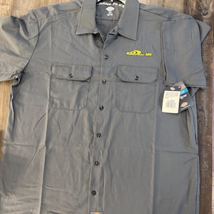 May include: Gray short-sleeve work shirt with two chest pockets and button-down closure. Features a yellow logo on the right chest and a tag. The shirt is labeled "Dickies Flex".
