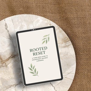 Puede incluir: Una tableta digital que muestra el texto "ROOTED RESET" con el subtítulo "A THREE-WEEK GUIDE TO NOURISHMENT, BALANCE & RENEWAL". La tableta está sobre una superficie con diseño de mármol, sobre un fondo texturizado de tono neutro.