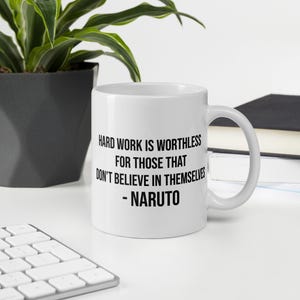 May include: White ceramic mug with a black handle. The mug features the quote "HARD WORK IS WORTHLESS FOR THOSE THAT DON'T BELIEVE IN THEMSELVES - NARUTO" in black text. The mug is on a white surface.