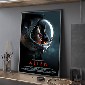 Puede incluir: Póster enmarcado de la película "Alien". Muestra un primer plano de una persona con un casco espacial, con el título de la película en rojo. El póster tiene una estética oscura y cinematográfica.
