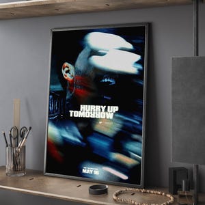 May include: Framed movie poster with the text "Hurry Up Tomorrow" in white. The poster features a blurred image of a person's face with blue and red tones. The release date "May 16" is also visible.