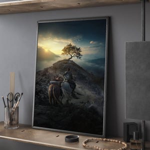 Puede incluir: Impresión artística enmarcada que representa a dos jinetes a caballo ascendiendo una montaña, con un árbol solitario en la cima. La obra presenta un cielo dramático con un sol poniente, creando un paisaje escénico.