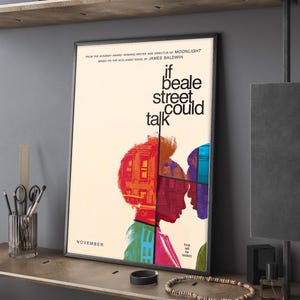 Pode incluir: Um cartaz de filme emoldurado para "If Beale Street Could Talk" com um fundo creme. O cartaz apresenta o texto do título e silhuetas de duas pessoas. O cartaz tem uma moldura preta e é exibido em uma prateleira de madeira.