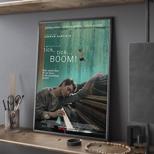 Może przedstawiać: Oprawiony plakat filmowy do filmu "tick, tick... BOOM!" z Andrew Garfieldem. Plakat ma turkusowe tło z pływającym mężczyzną i Garfieldem grającym na pianinie. Tekst zawiera tytuł filmu i "Netflix November 19".