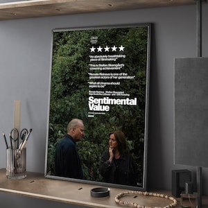 Könnte beinhalten: Ein gerahmtes Filmplakat für "Sentimental Value" mit zwei Personen vor einem grünen Hintergrund. Das Plakat enthält Filmkritiken und den Filmtitel. Das Plakat wird auf einem Holzregal ausgestellt.