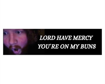 Puede incluir: Una pegatina rectangular con fondo negro y texto blanco que dice "LORD HAVE MERCY YOU'RE ON MY BUNS". El lado izquierdo de la pegatina presenta un primer plano del rostro de una persona con la boca abierta y expresión de sorpresa.