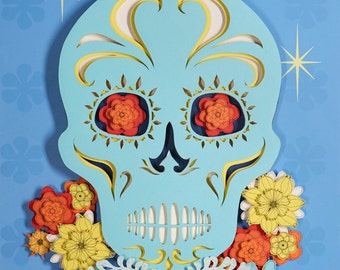 Könnte beinhalten: Ein blauer Papiermaché-Schädel mit gelben und weißen Details, umgeben von bunten Papierblumen. Der Schädel ist eine traditionelle Dekoration für den Tag der Toten.