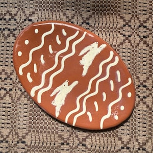 May include: Oval-shaped, terracotta-colored ceramic plate with a whimsical design. The plate features white wavy lines and two white rabbit illustrations. Small white dots are scattered across the surface, adding to the playful aesthetic. A decorative piece for the home.