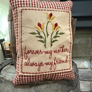 May include: A decorative pillow with a beige center featuring embroidered yellow and red flowers and the text "forever my mother always my friend." The pillow has a red and white checkered border.