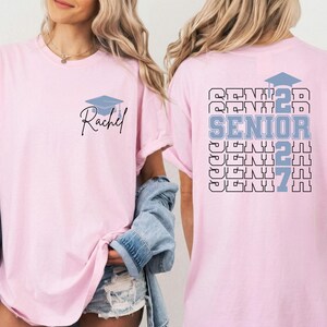 Senior class 2027 t shirt featuring bold graduation typography, personalized name customization and graduation cap graphic on a blue Comfort Colors shirt suitable for graduation parties and keepsake gifts. Graduation celebration shirt showcasing custom student name, senior year 2027 artwork and layered typography design printed on a comfortable blue Comfort Colors t shirt for high school graduates.
