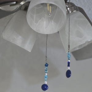 May include: A ceiling fan with four blades and three frosted glass light fittings. Decorative pull chains with blue and white beads and a dark blue orb are attached to the light fittings.