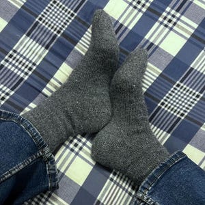 May include: A pair of mid-calf length socks in a heathered charcoal grey knit fabric. The socks feature a ribbed cuff at the top and a standard heel construction, worn with blue denim jeans that are visible at the ankles of the socks.