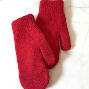 Puede incluir: Un par de manoplas de color rojo brillante con una superficie de punto difusa de textura suave y un diseño de puño acanalado. Las manoplas tienen una sección para el pulgar definida y una zona redondeada para la mano.