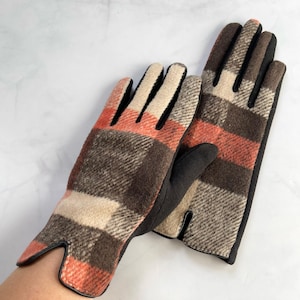 May include: A pair of plaid gloves in shades of brown, beige, and orange. The gloves feature black leather palms and trim, providing a classic and warm design. These gloves are designed for cold weather, offering warmth and style.