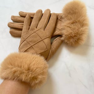 Könnte beinhalten: Ein Paar hellbraune Handschuhe mit einem Rautenmuster auf der Handrückseite. Die Handschuhe haben eine Kunstfellmanschette in passender hellbrauner Farbe. Die Handschuhe sind aus einem weichen, Wildleder-ähnlichen Material.
