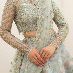 May include: A light blue and silver embellished formal gown. The bodice features intricate beadwork and a delicate net pattern on the sleeves. The skirt has a floral print with matching embellishments.