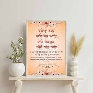 May include: A framed print with floral accents and text in a script. The text is in a foreign language, with an English translation below. The frame is a light wood colour, and the background is a peach colour.