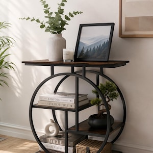 May include: A circular black metal console table with dark wood shelves. The unit features a round frame design with multiple storage levels holding books, a white vase with greenery, a framed mountain print, a candle, and a woven basket.