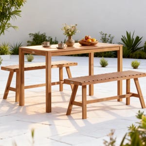 May include: A rectangular light brown wooden dining table with two matching slatted benches. The table surface holds two small ceramic cups on saucers, a ceramic vase containing white flowers, and a wooden bowl filled with assorted fresh fruit.