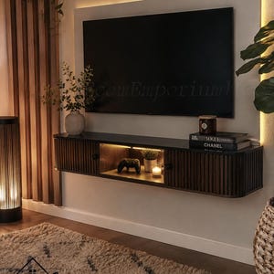 May include: A wall-mounted dark wood media console with vertical slats and a central open shelf featuring integrated LED lighting. The console is positioned beneath a flat-screen television mounted on a light-colored panel with backlighting.
