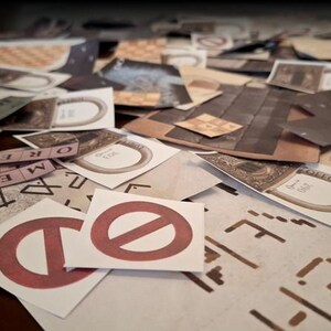 May include: A collection of game pieces, including cards with ring designs, strips of text, and cards with a red prohibition symbol. The pieces are scattered on a surface, suggesting a board game or puzzle.