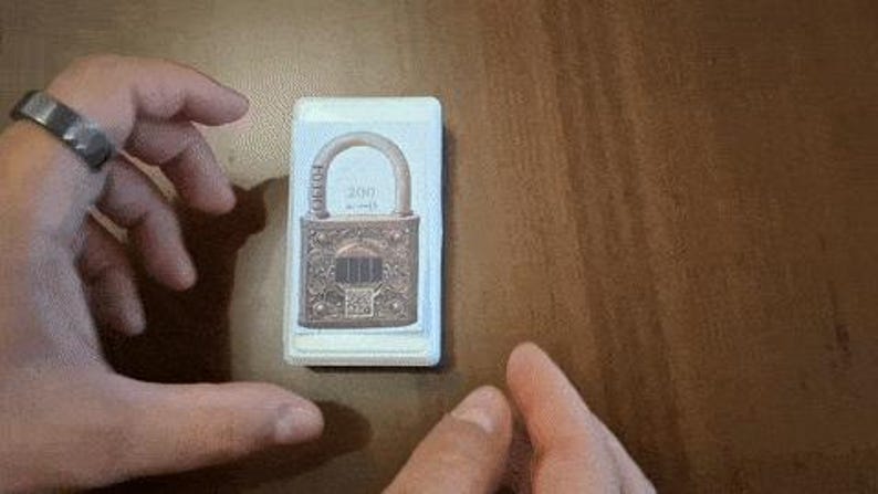May include: A rectangular card featuring a detailed illustration of a vintage padlock with a bronze finish. The padlock has an arched handle and intricate decorative patterns. The number "200" is visible on the card.