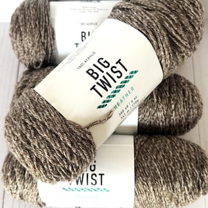 Puede incluir: Primer plano de varios ovillos de lana Big Twist Heather en color marrón. Cada ovillo tiene una etiqueta con el nombre de la marca, la composición de la fibra y el metraje. La lana es 100% acrílica, adecuada para tejer y hacer ganchillo.