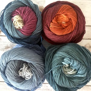 May include: Four skeins of yarn in various colors, including shades of blue, red, and orange. Each skein is tightly wound, revealing a lighter color in the center. Ideal for knitting and crochet projects.