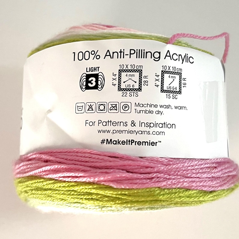 May include: A roll of multi-colored yarn with pink, green, and white strands. The label reads "100% Anti-Pilling Acrylic" and includes instructions for washing and care. The yarn is suitable for knitting and crochet projects.