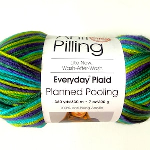 Puede incluir: Una madeja de hilo multicolor con rayas en verde lima, morado oscuro y azul turquesa. La etiqueta blanca dice Anti-Pilling, Everyday Plaid, Planned Pooling, 330 m, 200 g y 100% Anti-Pilling Acrylic con una pequeña foto de una persona.