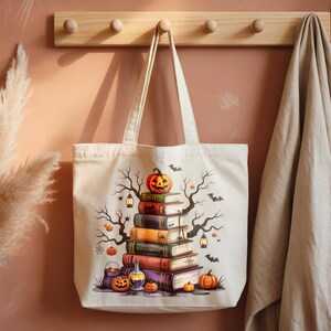 May include: A cream-colored tote bag featuring a Halloween-themed design. The design includes a stack of books topped with a carved pumpkin, bats, and spooky tree branches. Additional pumpkins, potion bottles, and lanterns complete the festive illustration.