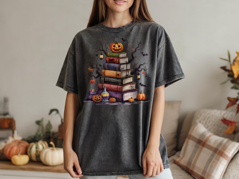 May include: Dark gray t-shirt featuring a Halloween-themed graphic. The design includes a stack of books topped with a jack-o'-lantern, bats, and pumpkins. The shirt has a vintage, washed look.