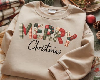 Puede incluir: Sudadera beige con las palabras "MERRY Christmas" en un diseño de patchwork. Las letras están hechas de varios patrones de cuadros y florales en rojo, verde y blanco. El texto está en una fuente de escritura negra.
