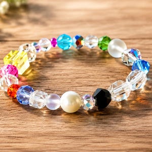May include: A circular bracelet composed of multi-colored beads including clear faceted crystals, a bright yellow cube, a solid white pearl-like sphere, a black faceted bead, and smaller vibrant blue, green, red, and pink accents arranged in a sequence.