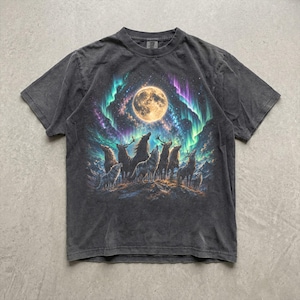 以下が含まれることがあります： チャコールグレーの半袖Tシャツ。満月と、その周囲を彩る鮮やかな紫と緑のオーロラ、そして星空の下の岩場に立つ狼と鹿の群れが描かれたグラフィックプリントが中央に施されています。