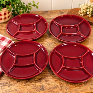 Peut inclure: Un ensemble de quatre assiettes circulaires en céramique rouge foncé, chacune dotée d'un compartiment central carré entouré de quatre sections incurvées, créant une disposition divisée pour servir des aliments avec une finition lisse et brillante.