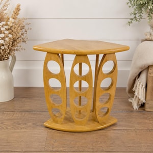 Peut inclure: Une table d'appoint en bois clair avec un dessus triangulaire et trois découpes ovales de chaque côté. La table a une base incurvée et est en bois de couleur claire.