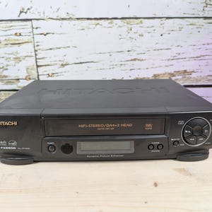 May include: Black Hitachi VHS player with HiFi-Stereo and DA4+2 Head features. The unit has a digital display and control buttons. The model number FX880B is visible on the front.