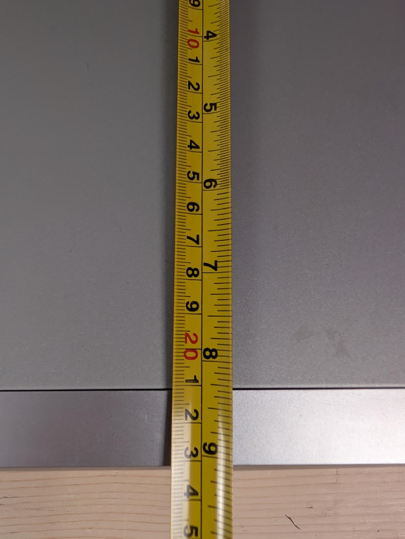 May include: A yellow and black measuring tape is positioned vertically against a gray surface. The tape shows measurements in inches, with clear markings and numbers. The image highlights the tape's precision and readability.