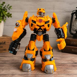 Peut inclure: Une figurine de robot jaune et noire avec des accents argentés sur les pieds et la tête. Le personnage présente un insigne Autobot rouge sur la poitrine, un visage mécanique aux yeux rouges et un gros canon noir fixé au bras droit.