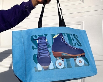 May include: A light blue tote bag with black handles, featuring a graphic of a roller skate and the word "SKATES" in teal. The roller skate is navy blue with brown wheels.