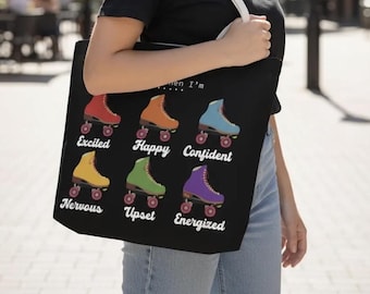 May include: Black tote bag featuring colorful roller skates with the words "Excited," "Happy," "Confident," "Nervous," "Upset," and "Energized." The bag has a white strap and is held by a person wearing a black shirt and blue jeans.