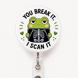 May include: A white badge reel with a cartoon frog holding an X-ray. The text on the badge reel reads "YOU BREAK IT, I SCAN IT". The frog is green with a black outline, and the X-ray is black and white.