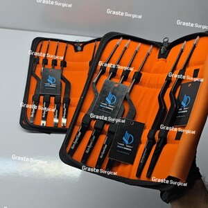 Op de afbeelding: Twee zwarte chirurgische instrumentensets met oranje interieurs. Elke set bevat meerdere instrumenten met zwarte handvatten en zilveren punten. De sets zijn gelabeld met de tekst "Graste Surgical" en "Micro Beyond Scissor".