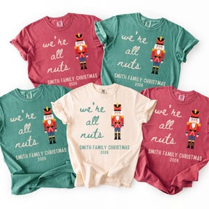 May include: Five short-sleeved t-shirts in red, green, and cream colors. Each shirt features a graphic of a nutcracker soldier and the text "we're all nuts" and "SMITH FAMILY CHRISTMAS 2026" printed in a casual, handwritten-style font.