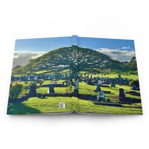 May include: Hardcover journal featuring a scenic photograph of a cemetery with a large tree and blue sky. The journal is open, displaying the image across both pages. The image is a landscape with green grass and headstones.