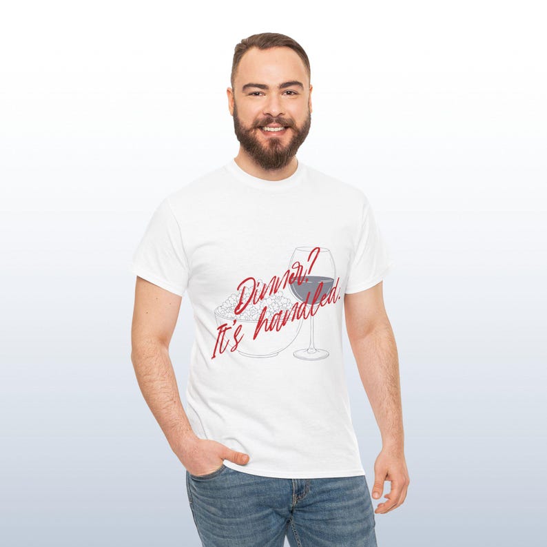 May include: White t-shirt featuring the text "Dinner? It's handled." in red script, alongside a wine glass and a plate of food. The shirt is worn by a person.
